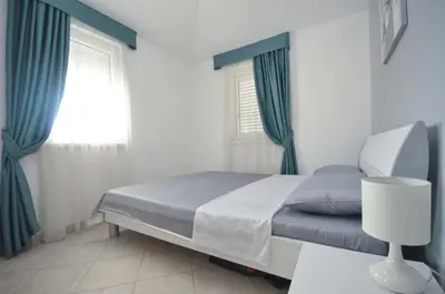 a bedroom with a bed with blue curtains and a window at Seaside Apartments Petrovac in Petrovac na Moru