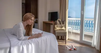 a woman sitting on a bed looking at her cell phone at Hotel Sato Conference & SPA Resort in Sutomore