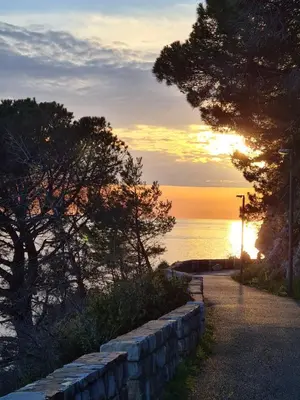 a sunset over the ocean with a stone wall at Palm Point Apartment in Petrovac na Moru