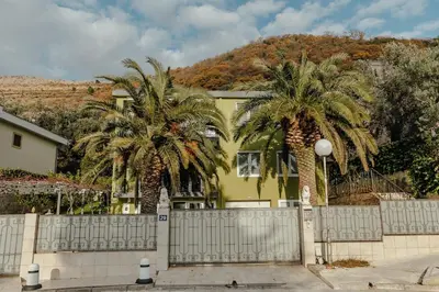 a yellow house with palm trees in front of it at Palm Point Apartment in Petrovac na Moru