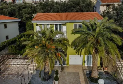 a yellow house with two palm trees in front of it at Olive Garden Apartment in Petrovac na Moru