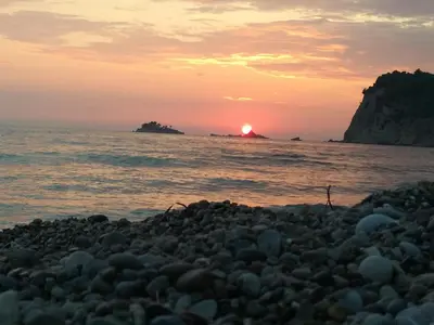 a sunset over the ocean with a rocky beach at Forest house in Sutomore