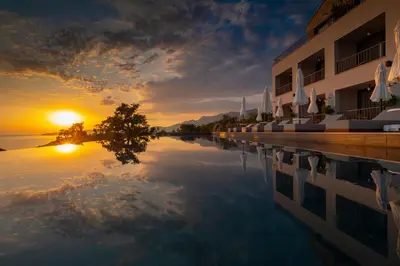 a reflection of the sunset in the water next to a building at Vivid Blue Serenity Resort in Sveti Stefan