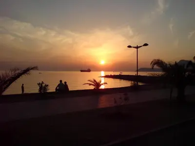 a sunset over the water with people walking on a sidewalk at Villa Jovanovic Sutomore in Sutomore