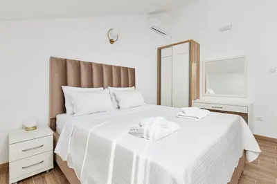a white bedroom with a large bed with a mirror at Apartments Rozer in Kotor