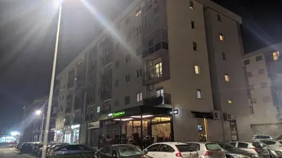 a tall building with cars parked in a parking lot at Guest House Mikeli (BESPL. DORUCAK)-(FREE BREAKFAST) in Podgorica