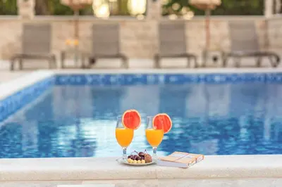 two glasses of juice and a plate of food next to a swimming pool at Luxury Apartments Queen in Petrovac na Moru