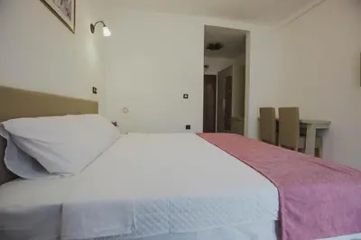 a bedroom with a white bed with a pink blanket on it at Hotel Dapčević in Cetinje