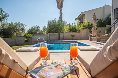 a table with two glasses of orange juice next to a swimming pool at Guest House Luksic in Bar