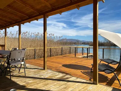 a wooden deck with chairs and a table on the water at Lake River House Ada Bojana in Ulcinj
