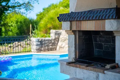 a swimming pool with an outdoor fireplace in a yard at Villa Robinson in Petrovac na Moru