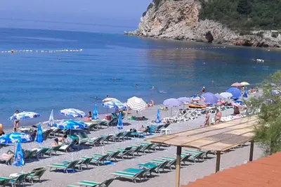 a beach with chairs and umbrellas and people on it at Two bedroom ap in the garden in Buljarica