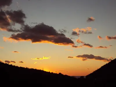 a sunset with clouds in the sky over a hill at Family Stone house with magical Sea View in Kaluđerac