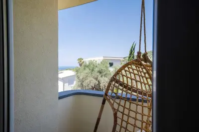 a rattan chair on a balcony with a view of the ocean at President Bungalows and Apartments in Utjeha