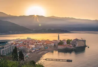 a view of a town on the water with the sunset at Apartments Inspiration in Budva