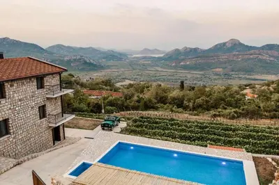 an outdoor swimming pool in front of a house with mountains at Apartments and Winery Djukovic in Virpazar