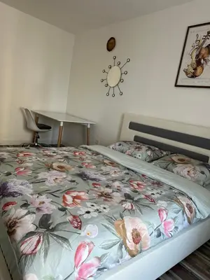 a bed with a floral comforter with a clock on the wall at Podgorica Great location in Podgorica