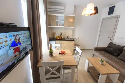 a living room with a table and a kitchen with a tv at Apartments Sarić in Bar