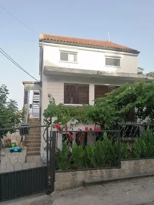 a white house with a black fence and flowers at Apartman Kosta in Utjeha