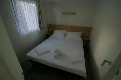 a small bedroom with a bed with white sheets and pillows at HILLS RESORT Beach, Bungalows and Bar - Velika Plaza Ulcinj in Ulcinj