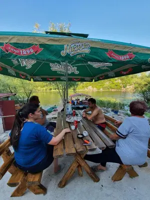 a group of people sitting at a picnic table under a green umbrella at Mali Raj Apartmani in Cetinje