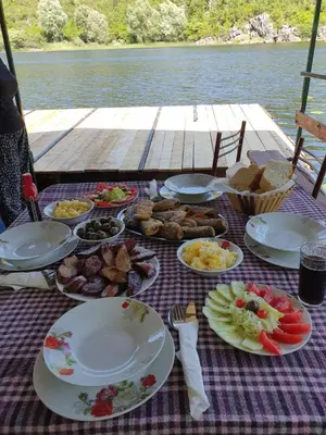 a picnic table with plates of food on a table near the water at Mali Raj Apartmani in Cetinje