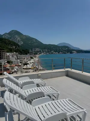 a row of white lounge chairs on a balcony overlooking the water at Hotel Kaligrosh in Sutomore