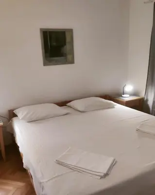 a white bed with two pillows and a tv on the wall at Apartmani Soljaga in Petrovac na Moru