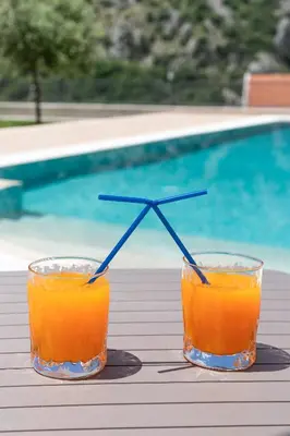 two glasses of orange juice on a table near a swimming pool at Sunset Rose in Kotor