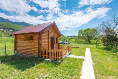 a small wooden cabin in a field with a parked car at Lovcen mountain cottages in Vratnica