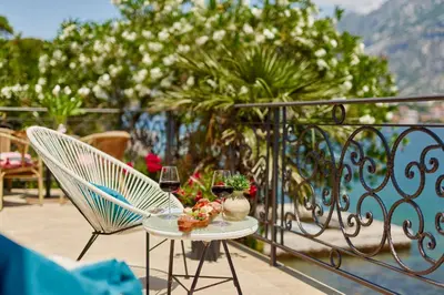 a table with a glass of wine and two chairs on a balcony at Apartment Aura with Sea View in Kotor
