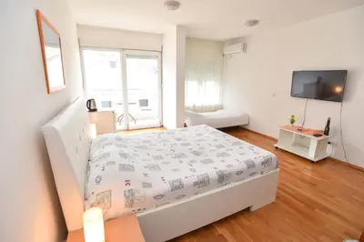 a white bedroom with a bed and a television at Modern Studio 200m from the Beach in Budva