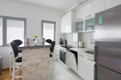 a kitchen with white appliances and a counter with chairs at City center lux apartment in Budva