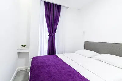 a white bed with a purple blanket in a bedroom at Miramare Apartments Pržno in Pržno