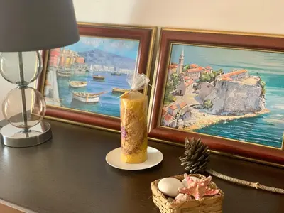 a table with a lamp a candle and a picture at Apartment Ruzmarin Petrovac in Petrovac na Moru