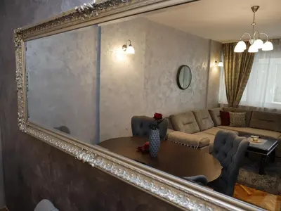a mirror reflecting a living room with a table and a couch at Apartment Mona in Podgorica