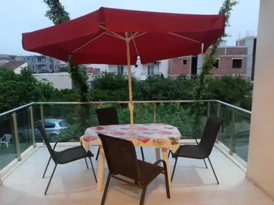 a patio table with a red umbrella on a balcony at Vila Arb in Ulcinj
