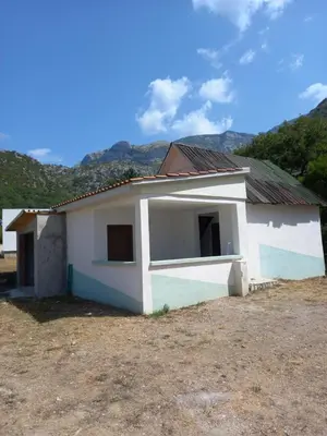 a small white house with mountains in the background at Vikendica in Čanj