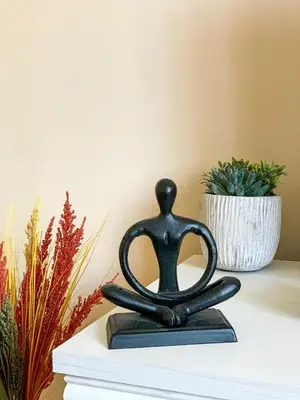 a statue of a person in a meditation pose next to a plant at Cute, spacious apt in the heart of the old town in Podgorica