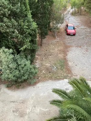 a red car parked on a dirt road next to trees at Stan na dan Bogdan in Podgorica