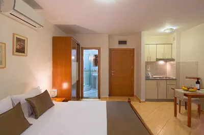 a bedroom with a white bed and a kitchen at Petrovac Holiday Apartments in Petrovac na Moru