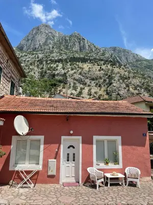a red house with a table and chairs and a mountain at Cozy Little House Kotor in Kotor