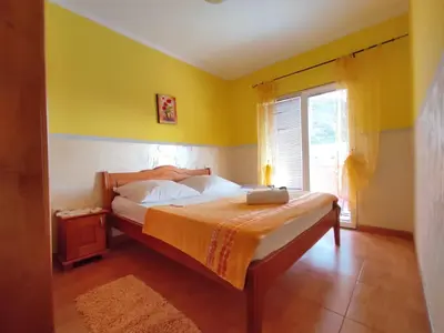 a bedroom with a bed with yellow walls and a window at Apartmani Tomić 4* in Rafailovici