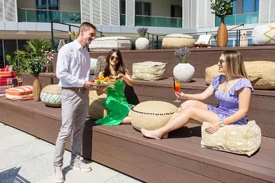 a man and two women sitting on a bench with drinks at Hotel TQ Plaza in Budva