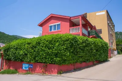 a red house behind a large green bush at Family Apartments Vukcevic in Čanj