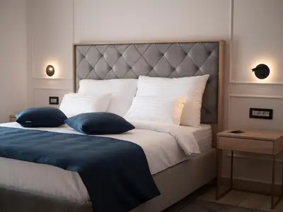 a bedroom with a large bed with white sheets and blue pillows at Hotel Idila Budva in Budva