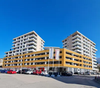 two tall buildings with cars parked in a parking lot at Apartment Juliette Budva in Budva