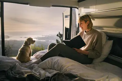 a woman sitting on a bed reading a book with a dog at Camper Montenegro and Recreational Vehicles in Budva