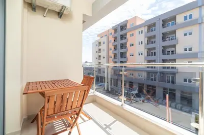 a balcony with a wooden chair and a view of a building at Modern Spacious Fully Equipped One Bedroom Apartment in Budva, Free Parking, Ideal for Long Stays in Budva