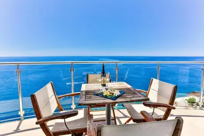 a table and chairs on a balcony with the ocean at Modern apartment with sea view in Dobra Voda, 95 m², Pool in Dobra Voda